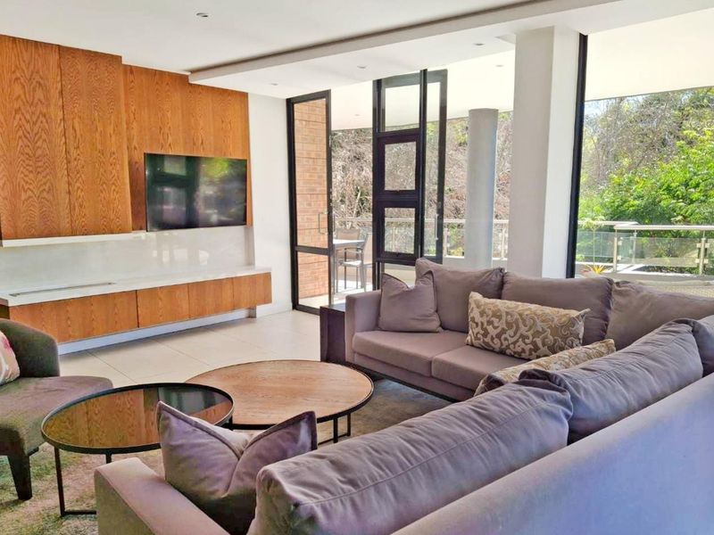 Modern living room featuring sleek built-in wooden cabinetry, large format floor tiles, and expansive glass doors opening to a balcony with natural views.