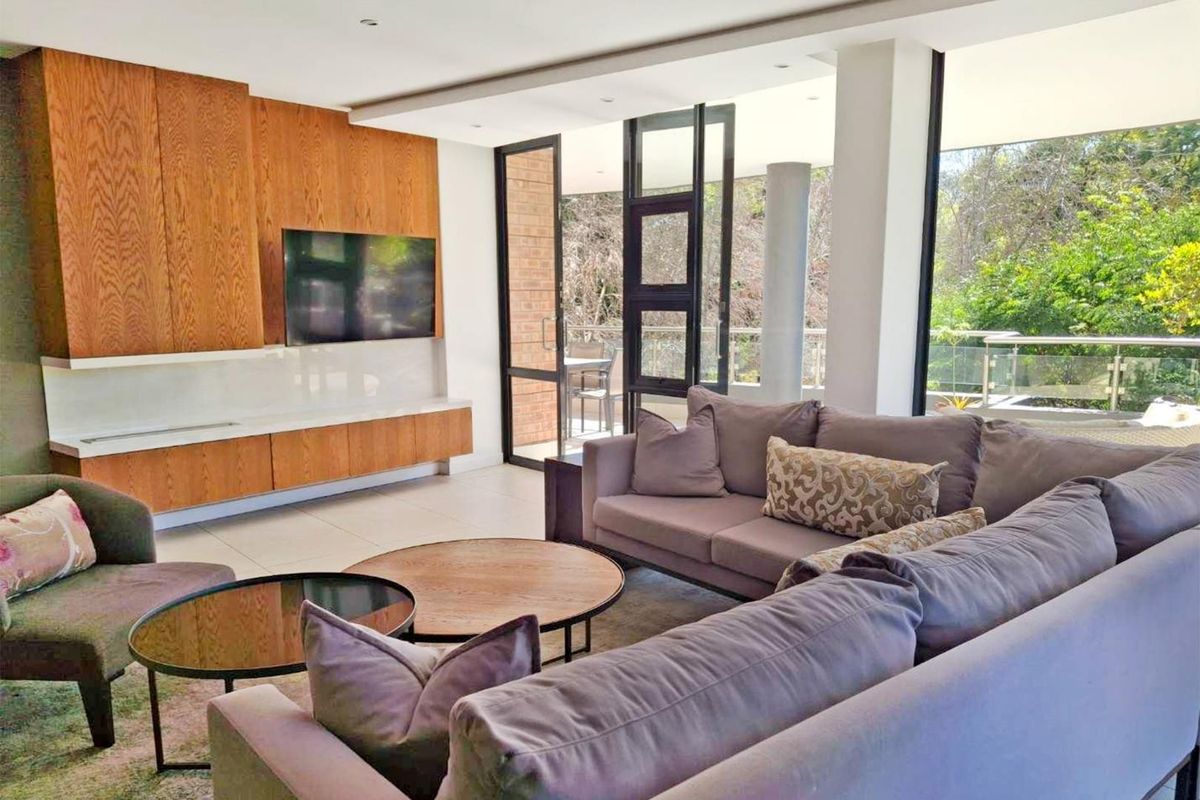 Modern living room featuring sleek built-in wooden cabinetry, large format floor tiles, and expansive glass doors opening to a balcony with natural views.