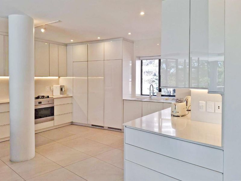 Modern kitchen featuring sleek white cabinetry, stone countertops, integrated appliances, and recessed lighting, complemented by large floor tiles and a structural column.
