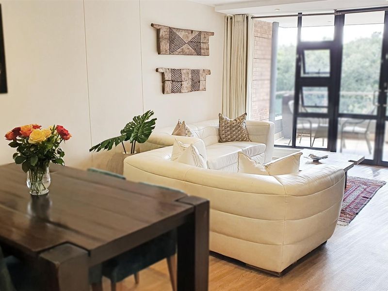 A bright open-plan living and dining area featuring laminate flooring and large sliding glass doors that provide access to an outdoor balcony.