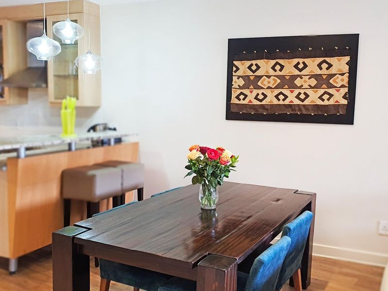 An open-plan living and dining area featuring a functional kitchen with wood cabinetry, stone countertops, and modern pendant lighting over a breakfast bar.