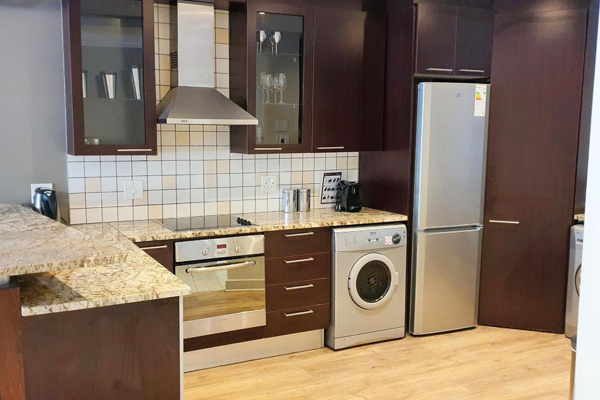 Modern kitchen featuring dark wood cabinetry, granite countertops, tiled backsplash, and integrated appliances including an oven, hob, and extractor fan.
