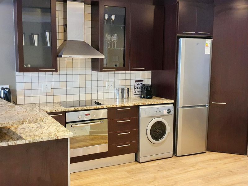 Modern kitchen featuring dark wood cabinetry, granite countertops, tiled backsplash, and integrated appliances including an oven, hob, and extractor fan.