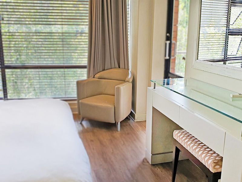 A well-lit bedroom featuring laminate flooring and large windows with venetian blinds, offering a bright and comfortable living space.