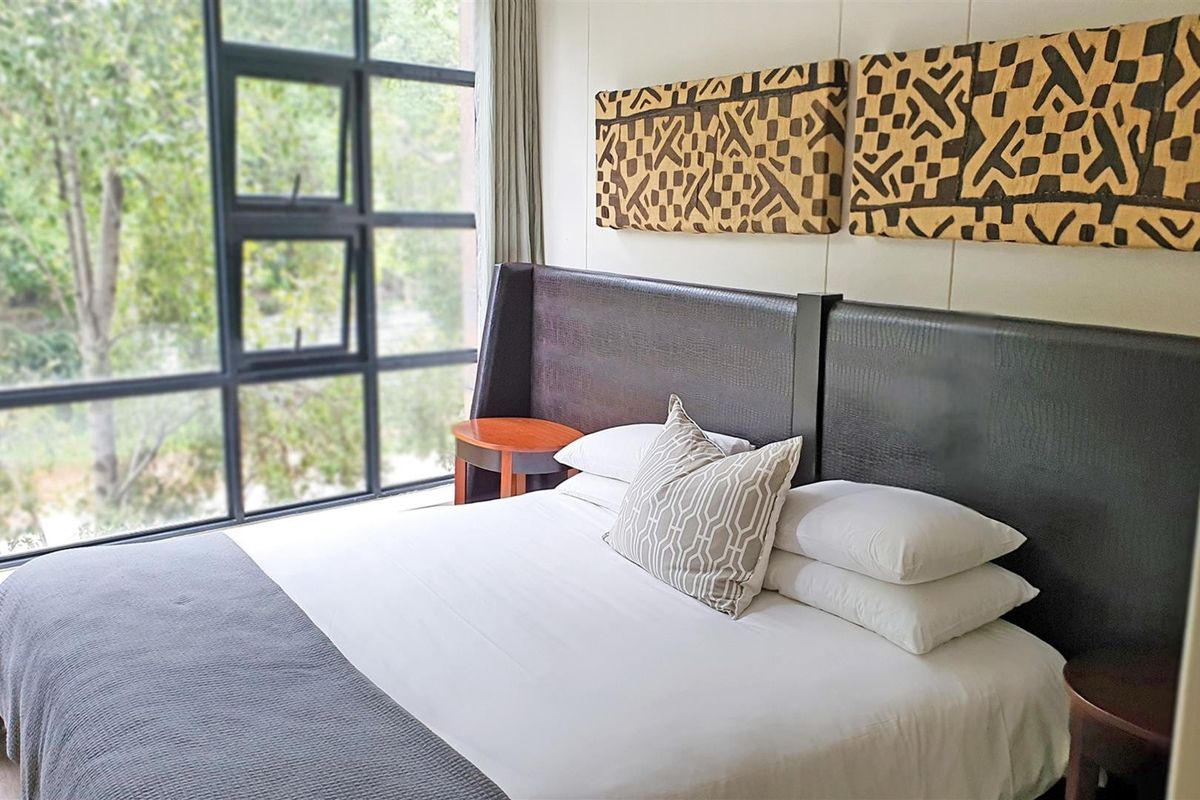 A well-lit bedroom featuring a large floor-to-ceiling window with a view of the surrounding greenery.