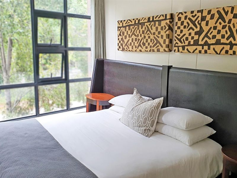 A well-lit bedroom featuring a large floor-to-ceiling window with a view of the surrounding greenery.