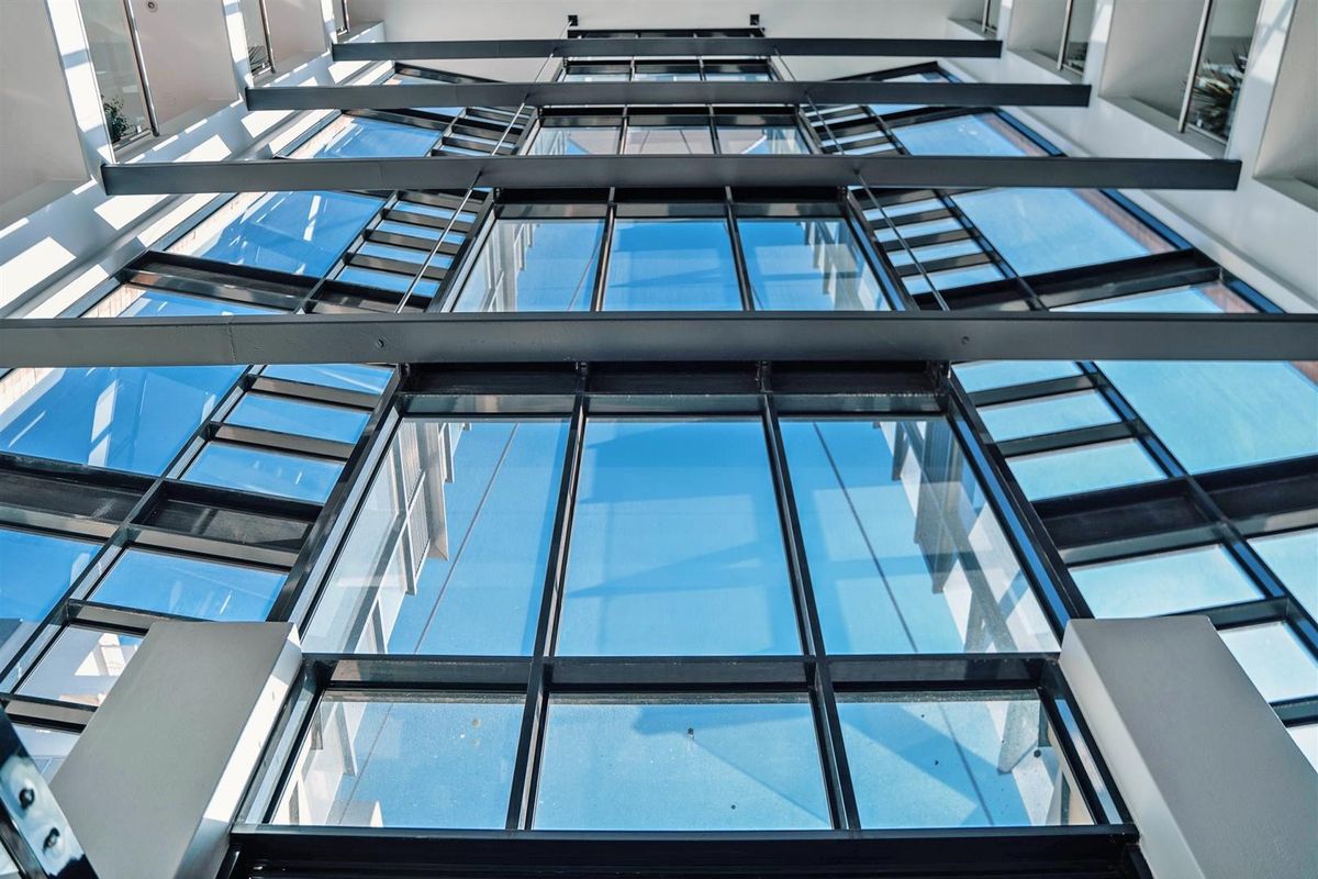 A low-angle view of a modern apartment building facade featuring extensive glass curtain walling and exposed steel structural beams.