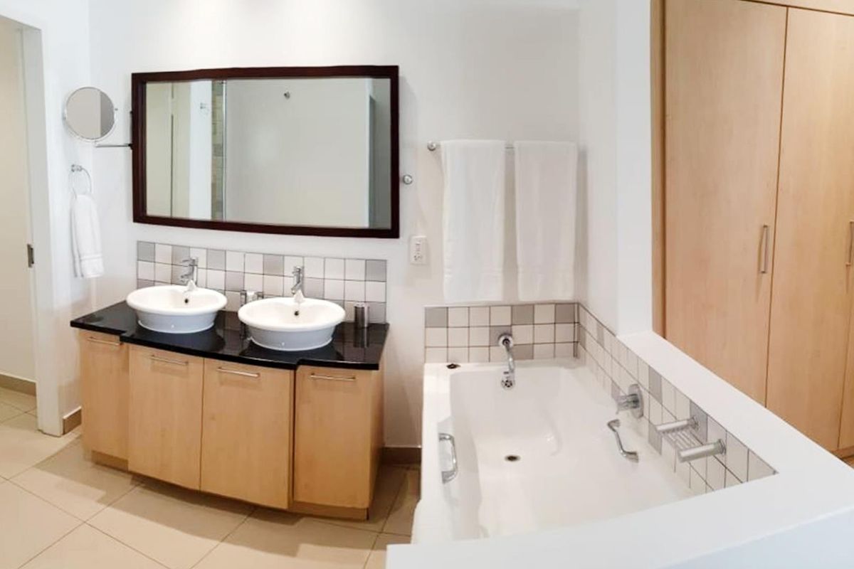 A well-maintained bathroom featuring a double vanity with vessel sinks, a built-in bathtub, and ample storage cabinetry with a neutral tiled finish.