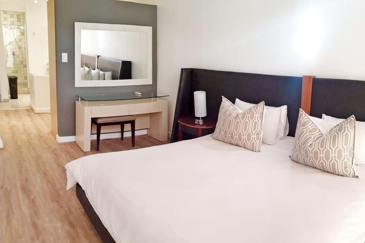 A well-maintained bedroom featuring light-toned laminate flooring and a modern built-in headboard, with an adjoining view into the bathroom area.