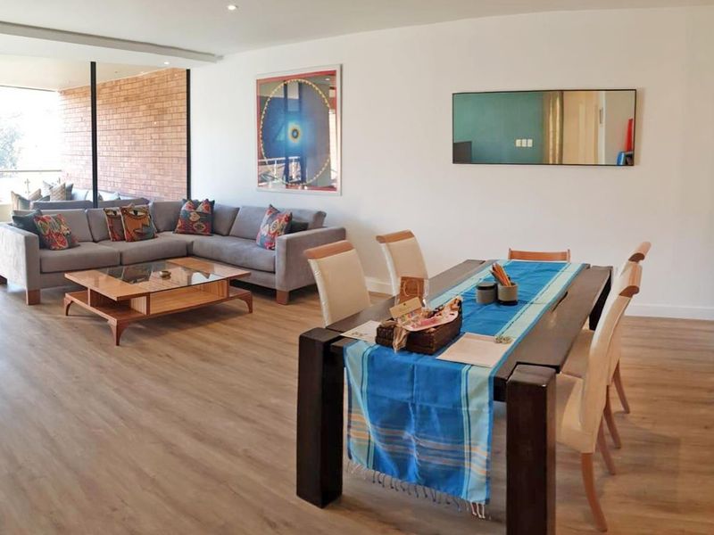Spacious open-plan living and dining area featuring modern laminate flooring, recessed lighting, and large sliding glass doors leading to an outdoor balcony.