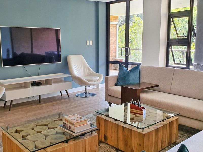 A bright and modern living room featuring laminate flooring, a blue accent wall, and large glass doors providing access to an outdoor balcony area.