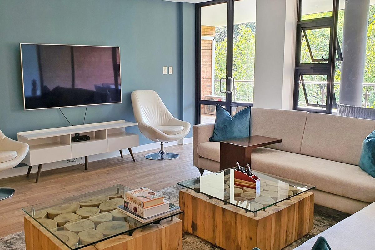 A bright and modern living room featuring laminate flooring, a blue accent wall, and large glass doors providing access to an outdoor balcony area.