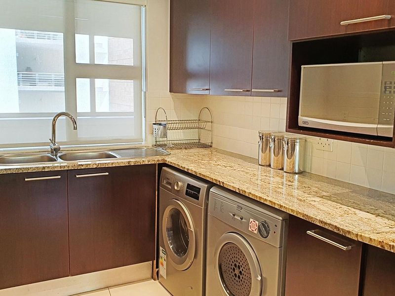 A functional kitchen featuring dark wood cabinetry, granite countertops, a stainless steel sink, and dedicated under-counter space for laundry appliances.