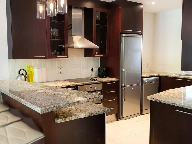 A well-maintained kitchen featuring dark wood cabinetry, granite countertops, a tiled backsplash, and built-in stainless steel appliances.