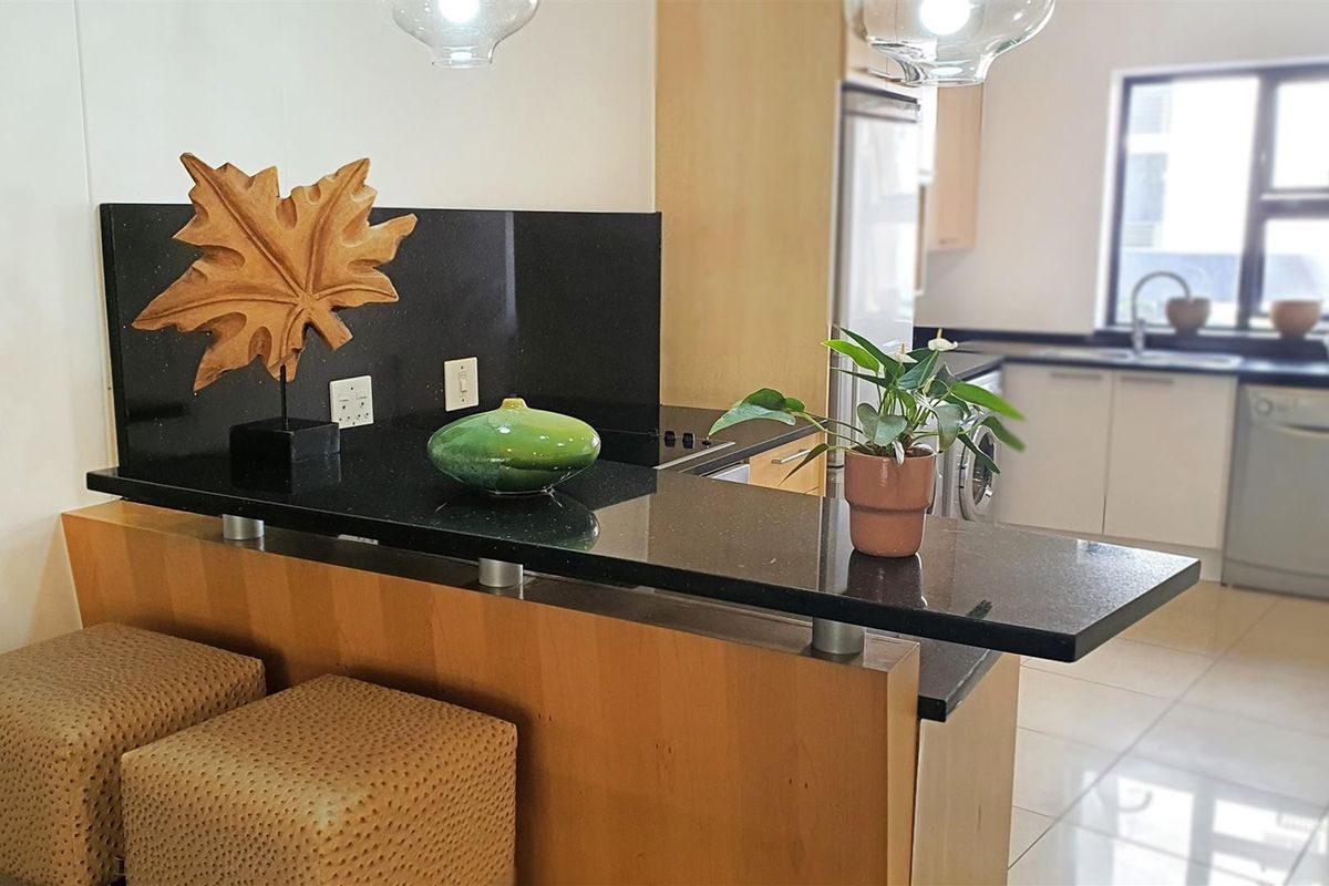 A functional kitchen featuring a breakfast bar with granite countertops, light wood cabinetry, and an integrated sink area with tiled flooring.