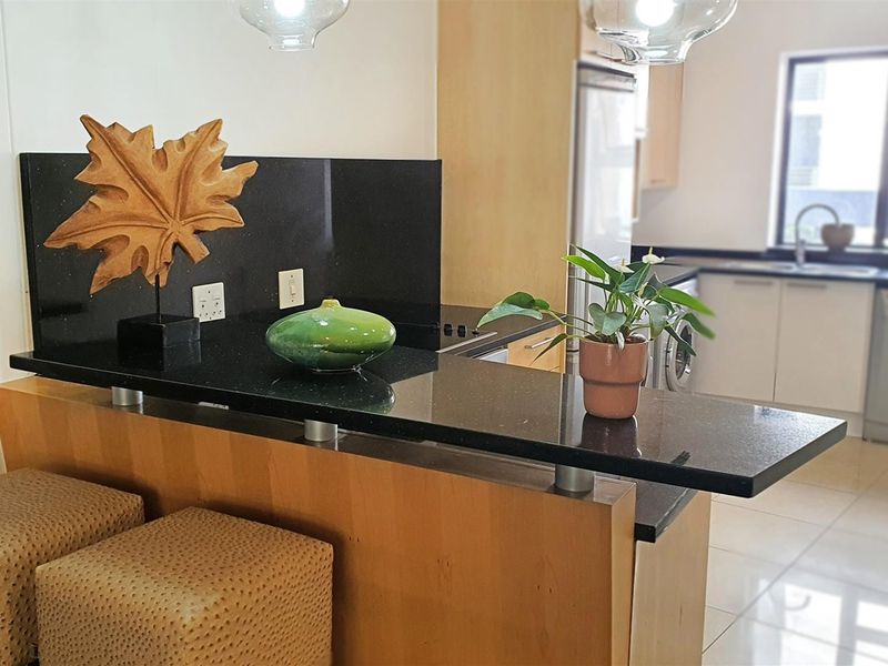 A functional kitchen featuring a breakfast bar with granite countertops, light wood cabinetry, and an integrated sink area with tiled flooring.