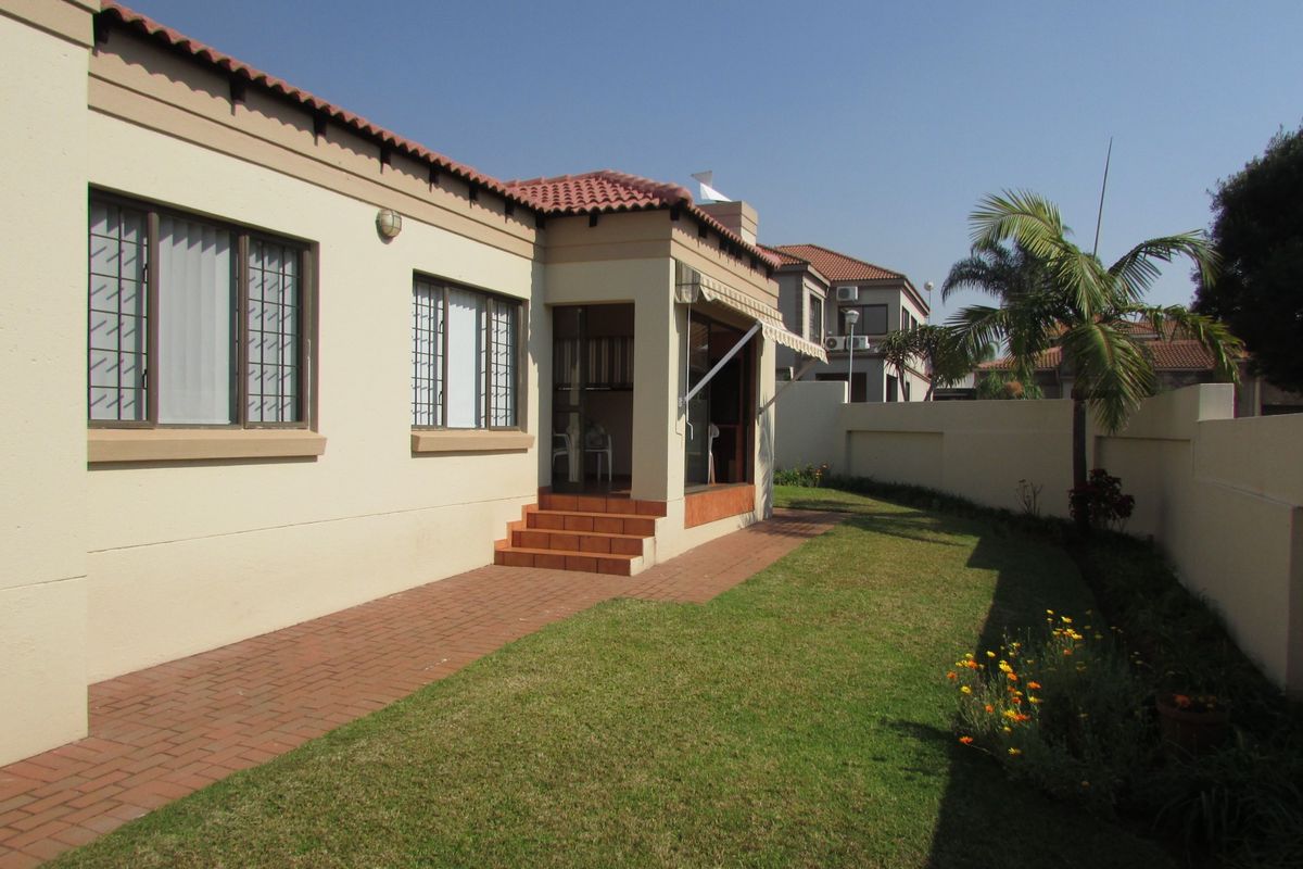 Rear view of the duet property featuring a paved walkway, a small lawn, terracotta steps leading to the entrance, and a retractable patio awning.