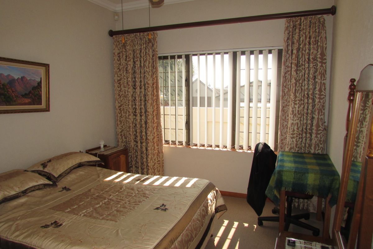 A bedroom featuring carpeted flooring, a ceiling fan, and a window fitted with vertical blinds and security bars.