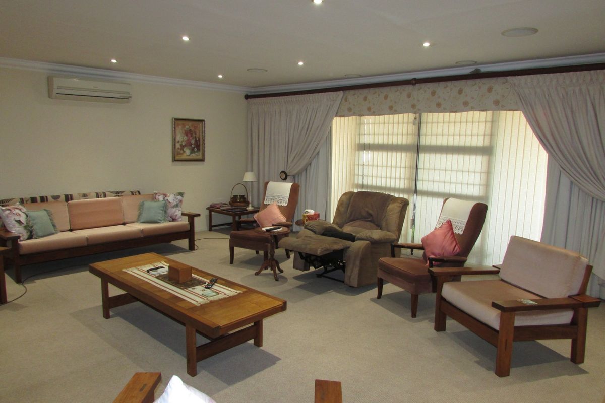 Spacious living room featuring recessed downlighting, wall-mounted air conditioning, and large sliding glass doors with vertical blinds for natural light control.
