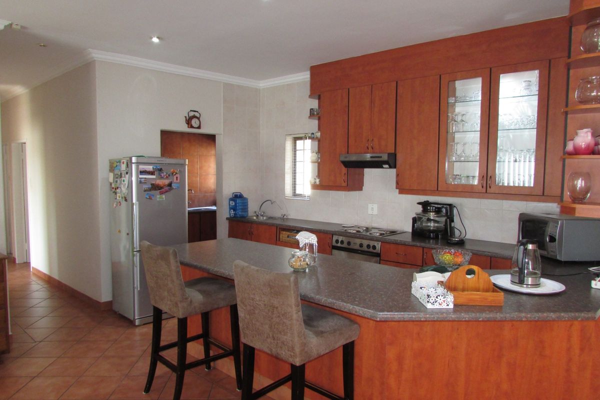 A functional kitchen featuring wooden cabinetry, laminate countertops, a breakfast nook, and tiled flooring, with an adjacent scullery area visible.