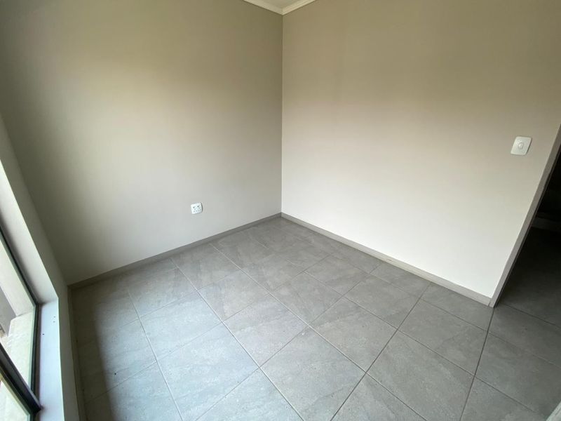 A clean, empty bedroom featuring neutral wall paint and modern grey floor tiles, providing a versatile space ready for personalization.