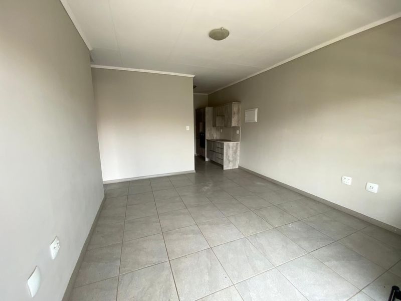 An empty open-plan living and kitchen area featuring neutral wall tones, tiled flooring, and built-in kitchen cabinetry.