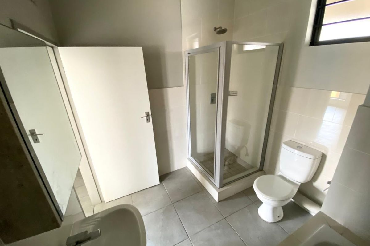 A functional bathroom featuring a shower enclosure, toilet, and pedestal basin with neutral wall and floor tiling.
