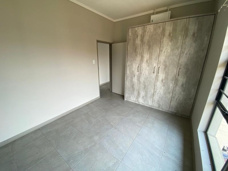A clean, empty bedroom featuring neutral tiled flooring and modern built-in cupboards with a wood-look finish.