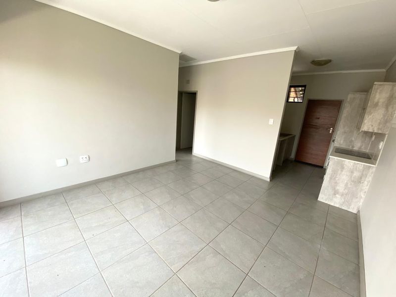 An open-plan living and kitchen area featuring neutral wall tones, large format floor tiles, and a compact kitchen with built-in cabinetry and hob.