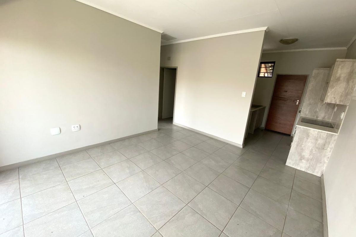 An open-plan living and kitchen area featuring neutral wall tones, large format floor tiles, and a compact kitchen with built-in cabinetry and hob.