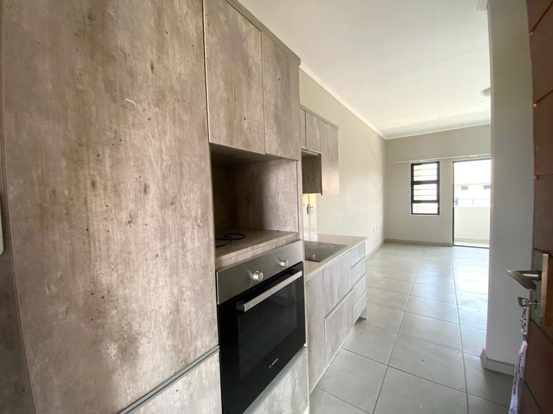 Modern open-plan kitchen featuring concrete-look cabinetry, built-in oven and hob, leading into a bright living area with tiled floors and balcony access.