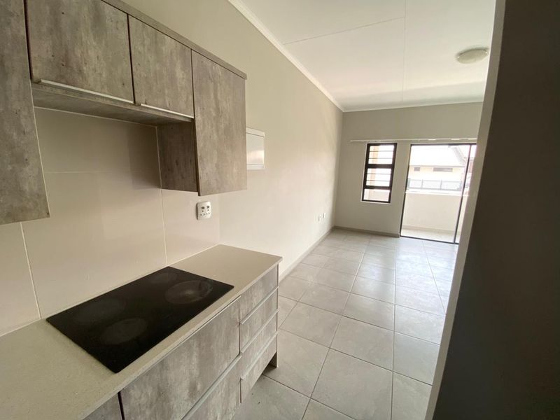 Modern open-plan kitchen and living area featuring contemporary cabinetry, electric hob, tiled flooring, and direct access to a balcony.
