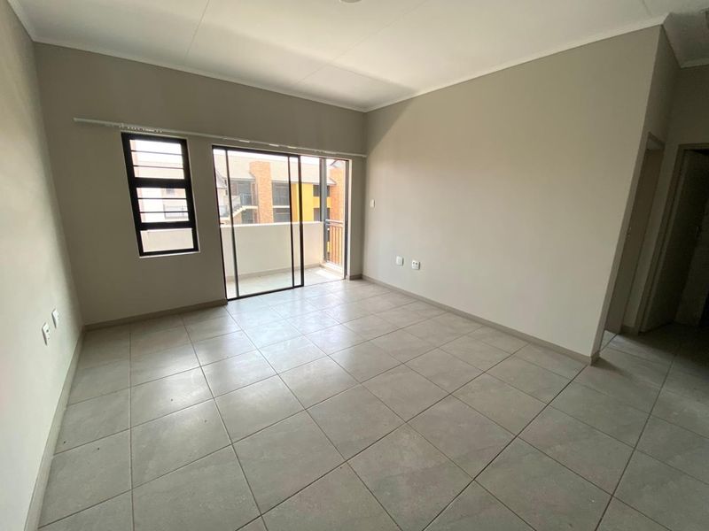 A bright, empty living area featuring neutral tiled flooring and a sliding glass door providing access to a private balcony.