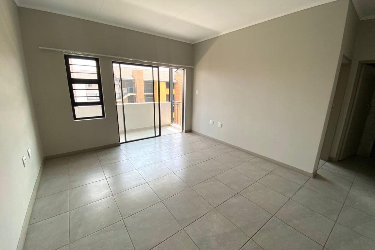 A bright, empty living area featuring neutral tiled flooring and a sliding glass door providing access to a private balcony.