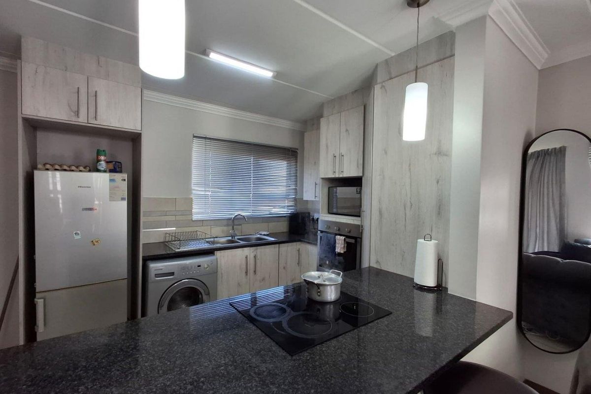 Modern kitchen featuring light wood-grain cabinetry, dark granite countertops, integrated electric hob, built-in oven, and functional laundry space with plumbing for a washing machine.