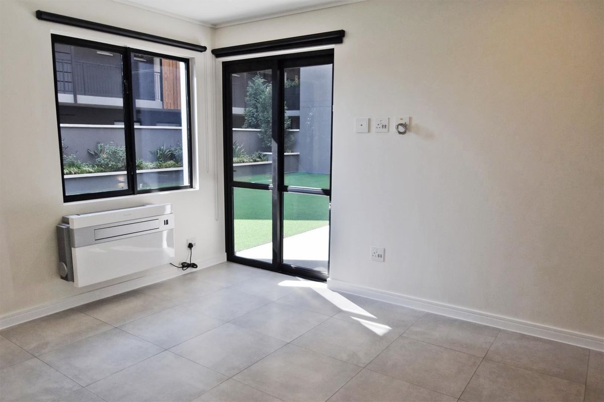 A bright, empty living area featuring modern tiled flooring, a wall-mounted air conditioning unit, and direct access to an outdoor patio through sliding glass doors.