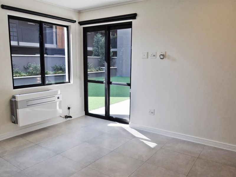 A bright, empty living area featuring modern tiled flooring, a wall-mounted air conditioning unit, and direct access to an outdoor patio through sliding glass doors.