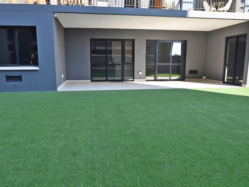 A well-maintained rear exterior featuring a covered patio with tiled flooring and sliding glass doors leading to a spacious artificial turf lawn.