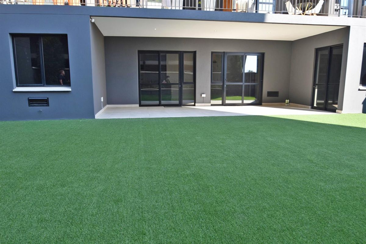 A well-maintained rear exterior featuring a covered patio with tiled flooring and sliding glass doors leading to a spacious artificial turf lawn.