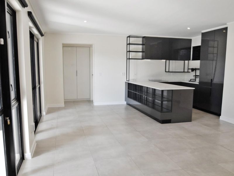 Modern open-plan kitchen and living area featuring sleek dark cabinetry, stone countertops, tiled flooring, and large sliding glass doors leading to the exterior.