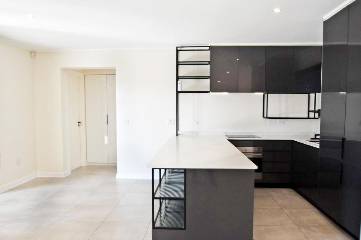 Modern kitchen featuring sleek dark cabinetry, stone countertops, integrated shelving, and high-quality built-in appliances, set against a neutral tiled floor.