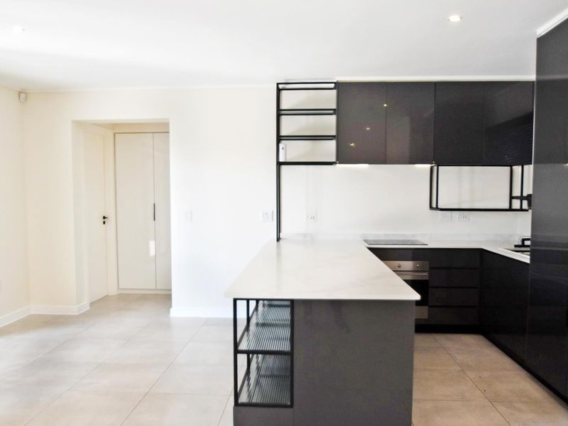 Modern kitchen featuring sleek dark cabinetry, stone countertops, integrated shelving, and high-quality built-in appliances, set against a neutral tiled floor.