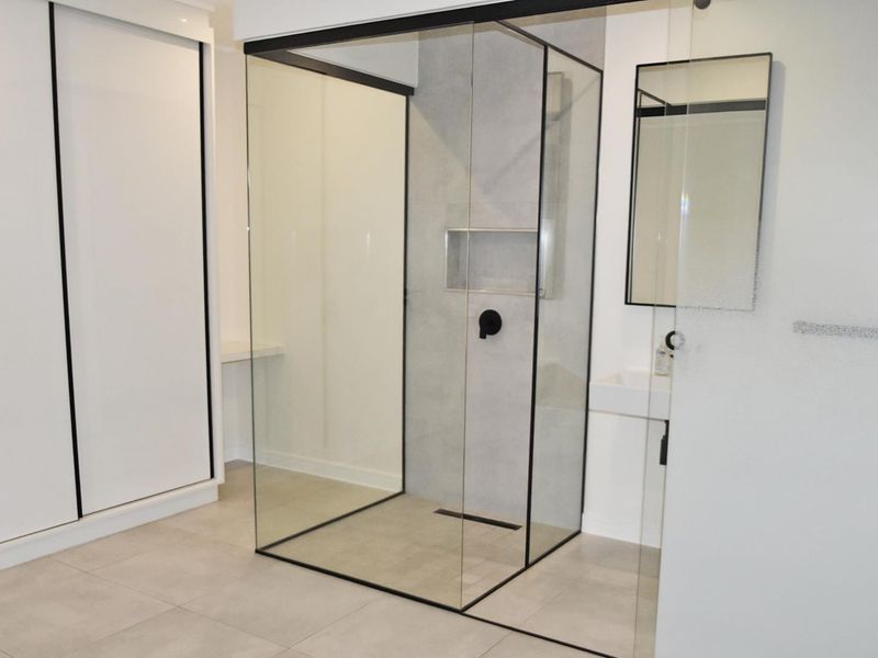 Modern bathroom featuring a walk-in shower with black-framed glass, a recessed niche, wall-mounted basin, and built-in storage cabinetry.
