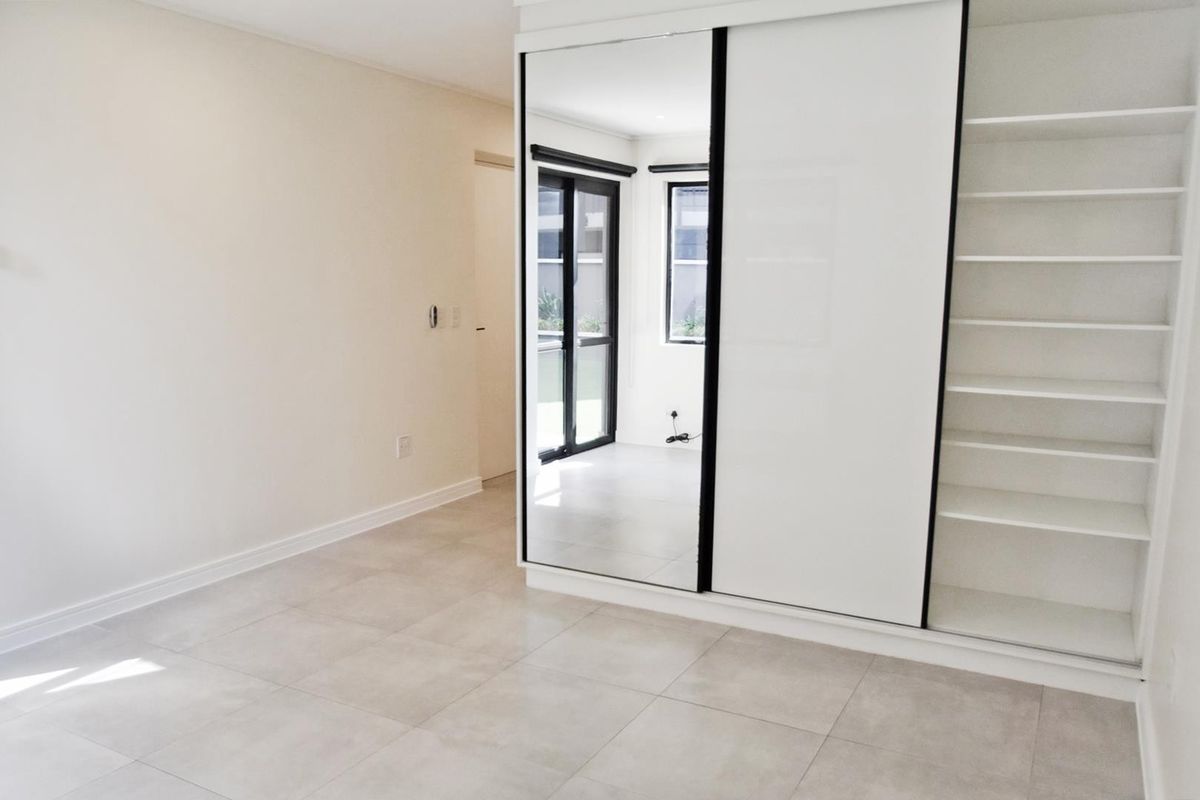A bright, empty bedroom featuring modern tiled flooring and a large built-in wardrobe with sliding mirror doors and integrated shelving.