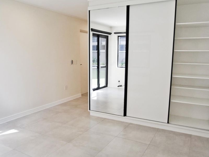 A bright, empty bedroom featuring modern tiled flooring and a large built-in wardrobe with sliding mirror doors and integrated shelving.