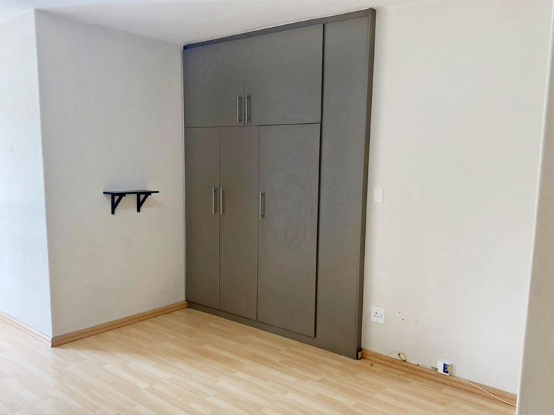 A bright bedroom featuring neutral walls, light laminate flooring, and floor-to-ceiling built-in cupboards providing ample storage space.