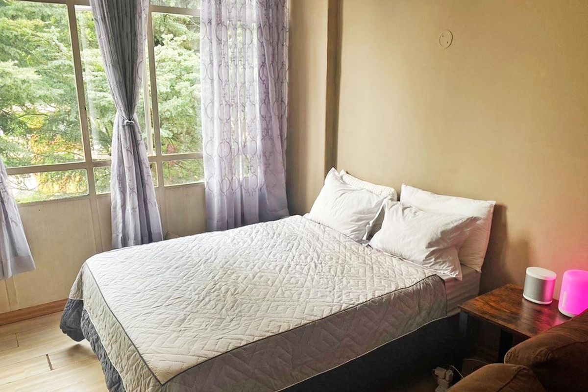 A bedroom featuring laminate flooring and a large window providing natural light and a view of the surrounding greenery.