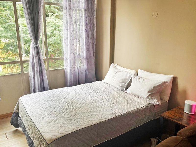 A bedroom featuring laminate flooring and a large window providing natural light and a view of the surrounding greenery.