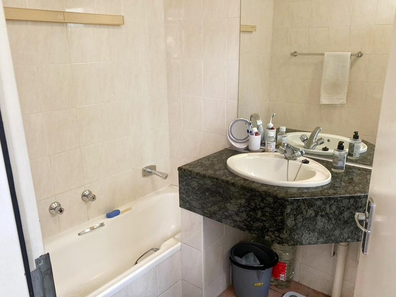A functional bathroom featuring a built-in bathtub, a vanity with a drop-in sink, and wall-mounted mirror, offering a dated but practical layout.