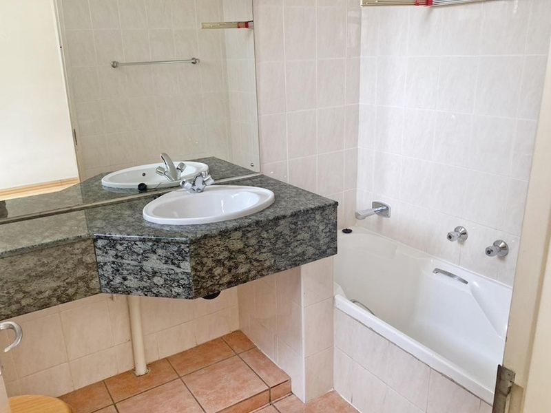 A functional bathroom featuring a granite vanity with a drop-in basin, a built-in bathtub, and neutral wall tiling.